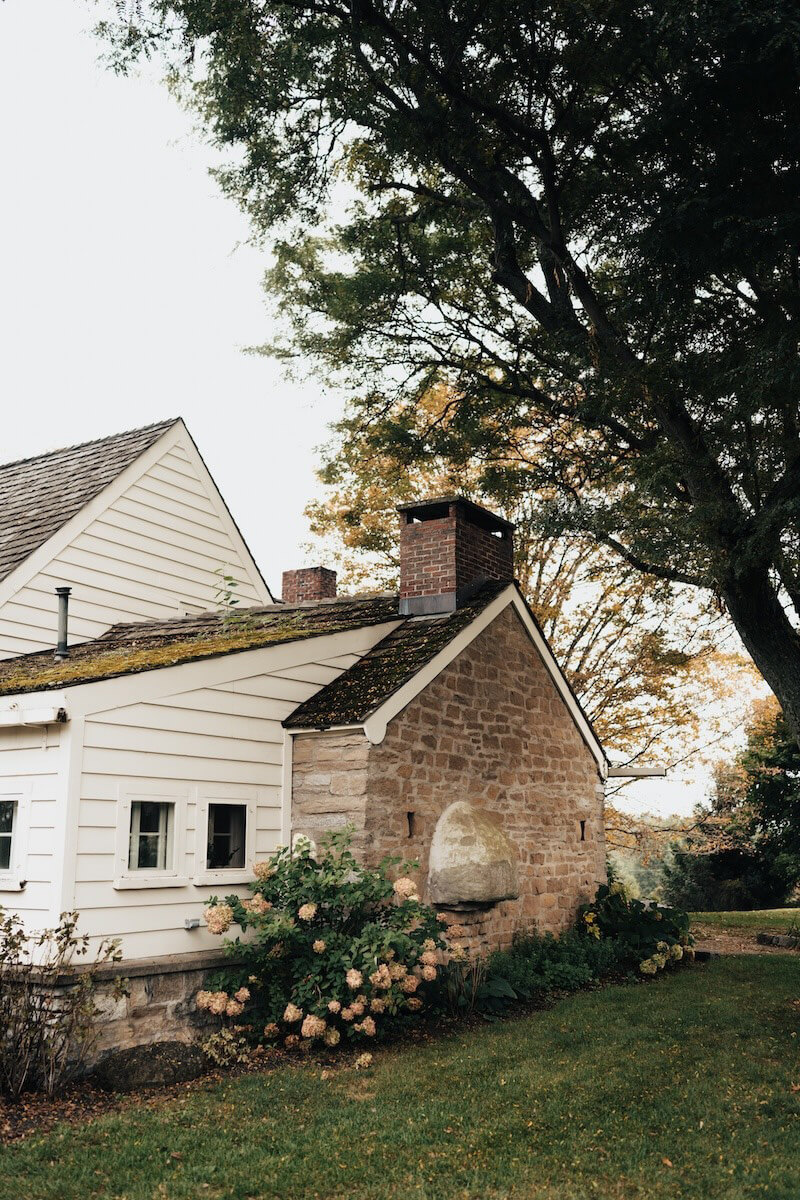 White house with beautiful brick chimney surrounded by flowers and trees.
