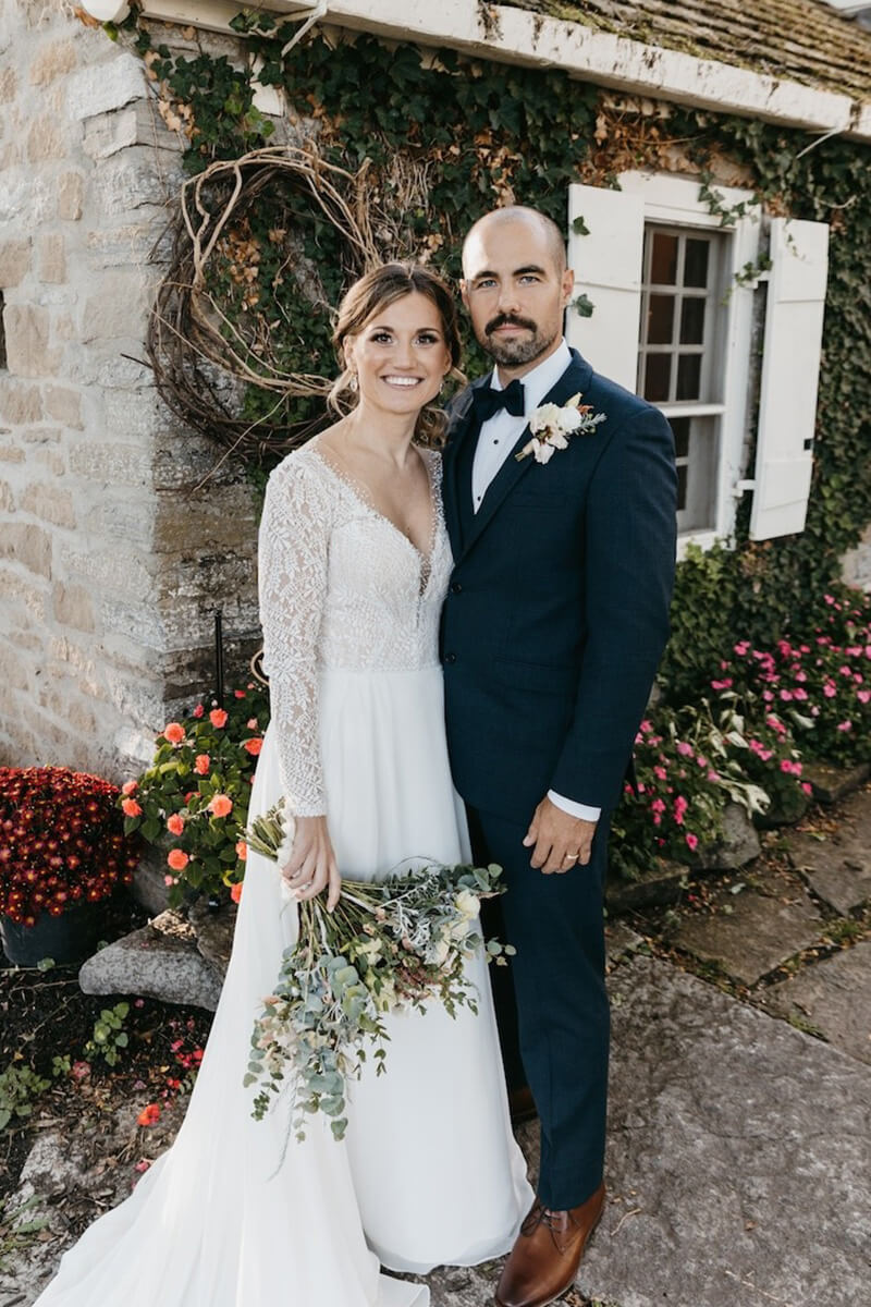 Bride and groom pose for wedding photo while holding beautiful bouquet.