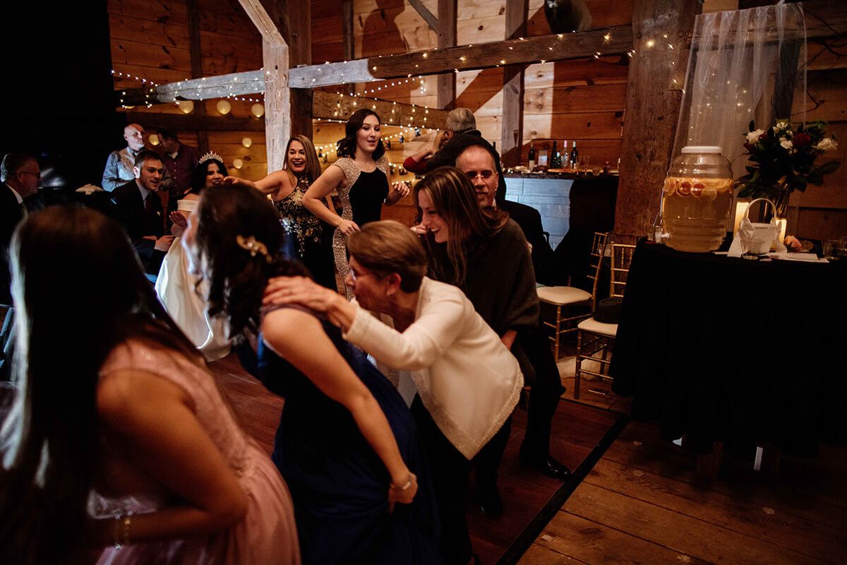 Wedding party partaking in conga line on dance floor inside scenic rustic barn.