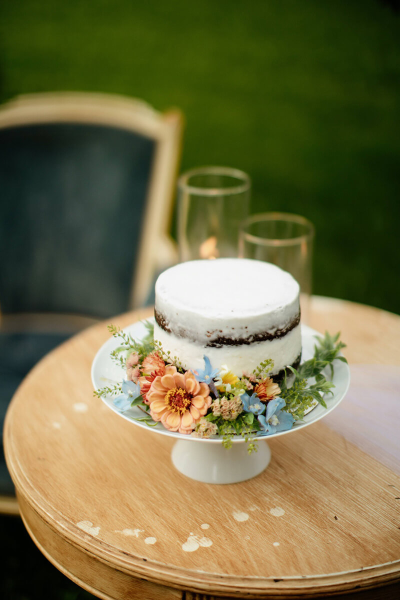 Close up of beautiful wedding cake in dish surrounded by orange and blue flowers.
