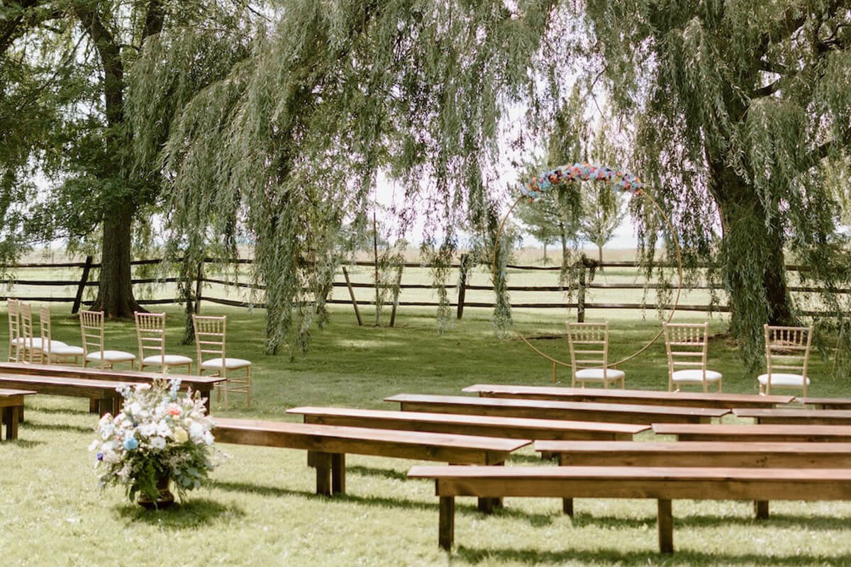 Outdoor wedding ceremony with rustic benches surrounded by trees in field.