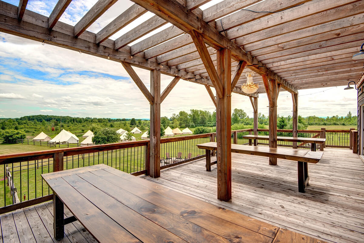Rustic barn deck overlooking scenic field with tents and a wood fence.