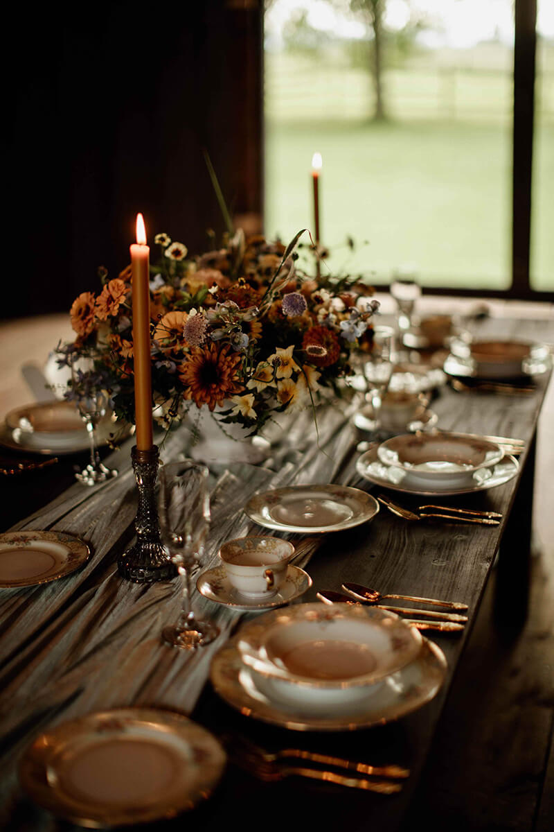 Intimate dining table lit with candles prepared to be served inside rustic barn wedding venue.